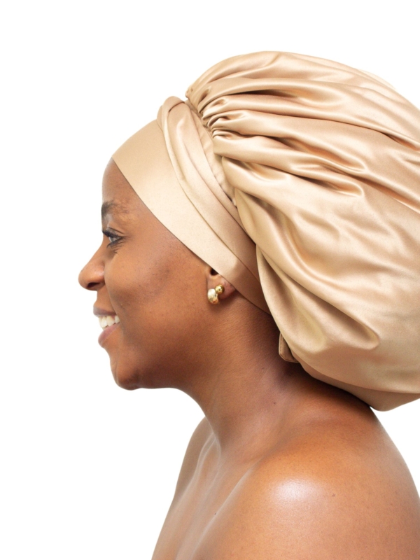 Woman wearing oversized soft gold satin bonnet for overnight natural hair protection.