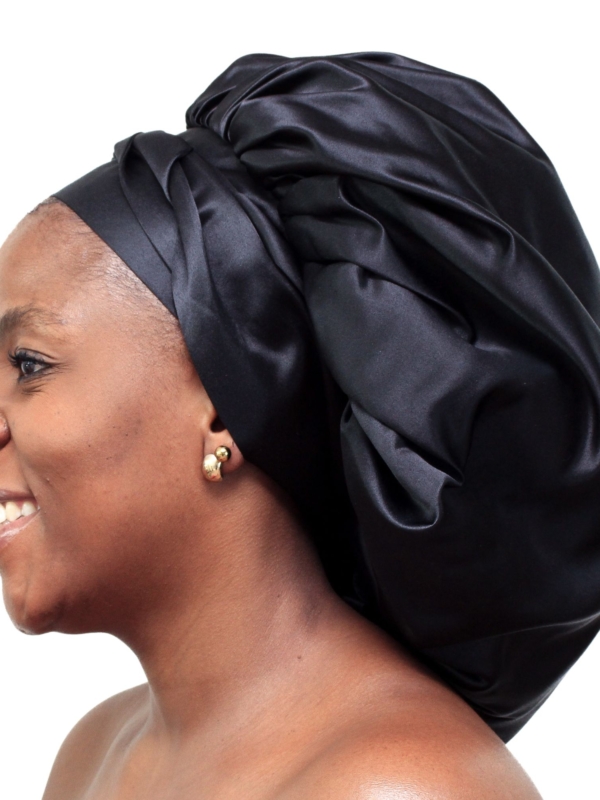 Woman wearing oversized black satin bonnet designed for overnight luxury hair protection