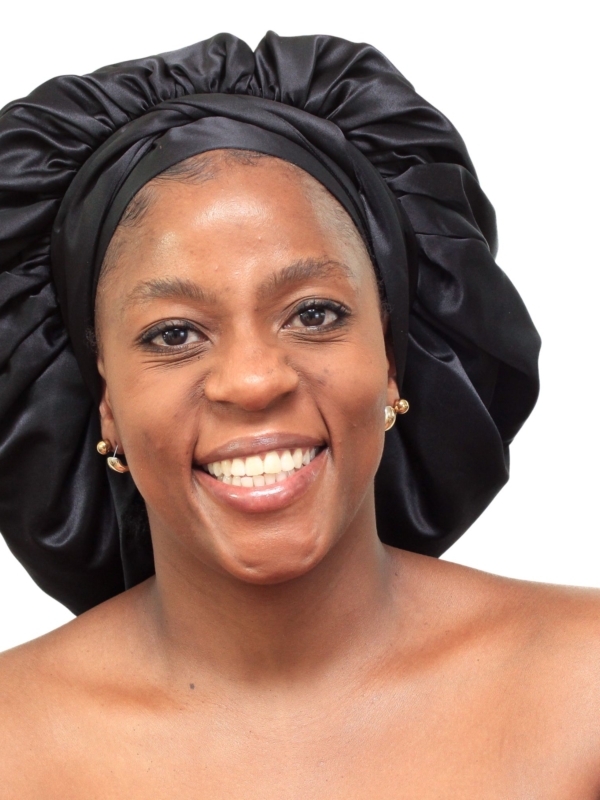 Woman wearing oversized black satin bonnet designed for overnight luxury hair protection