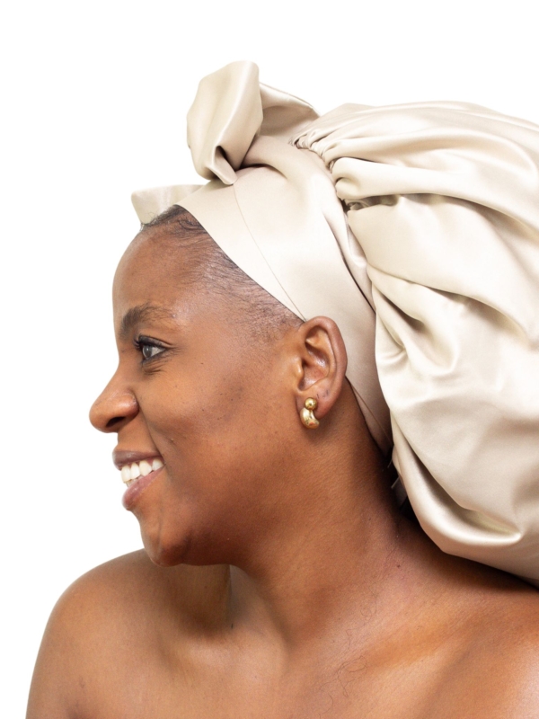 Woman wearing oversized champagne satin bonnet with soft structured luxury silhouette.