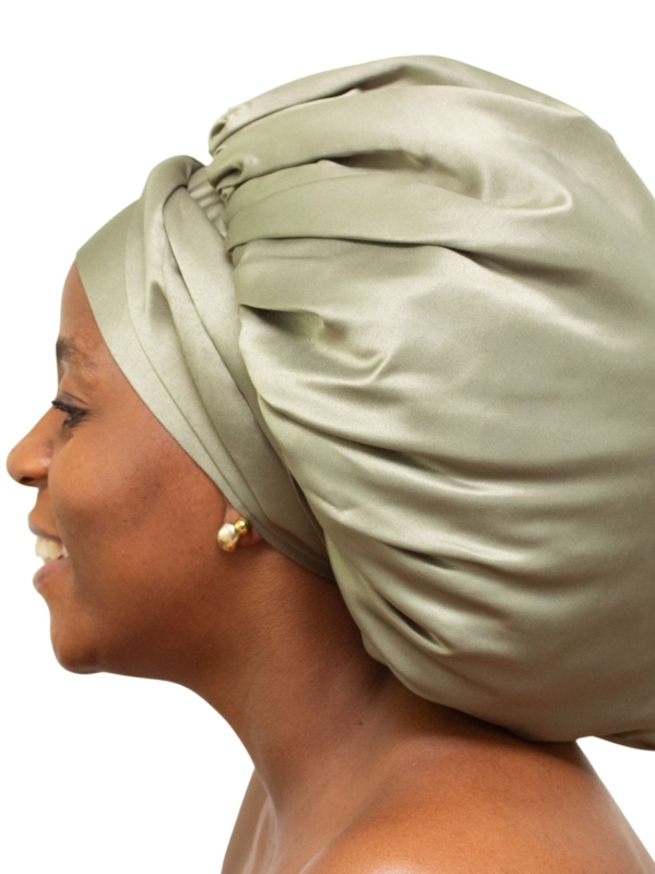 Woman wearing oversized deep olive satin bonnet designed for luxury natural hair protection.