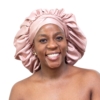 Woman wearing oversized blush pink satin bonnet designed for luxury overnight natural hair protection.